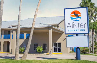 Exterior of Alister Square Inn with palm trees, blue balconies, and a sunny sky in Port Aransas
